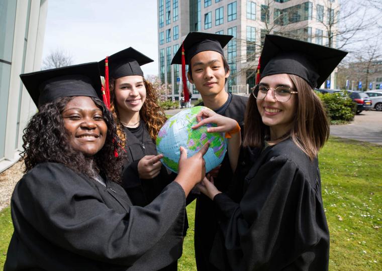 Students with a graduation hat pointing at the Netherlands on a globe