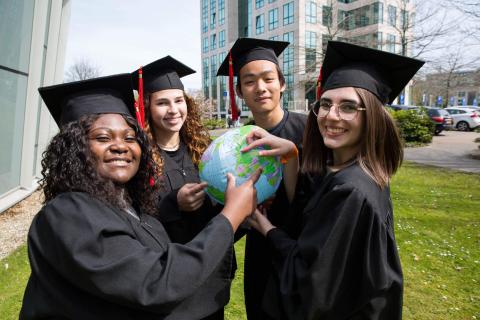 Students with a graduation hat pointing at the Netherlands on a globe